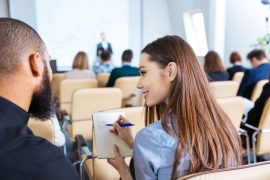 Back view of two young smiling people writing and talking on business meeting in conference hall